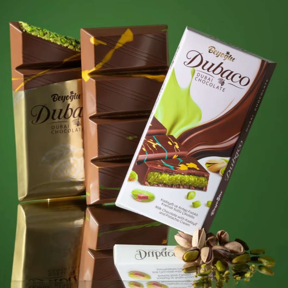 Stacked chocolate bars include one in gold wrapping and another in white packaging labeled "Dubaco," with pistachios hinting at a luscious pistachio cream filling inside the Beyoglu - Dubaco Premium Dubai Chocolate Bar - 200g. Stacked chocolate bars include one in gold wrapping and another in white packaging labeled "Dubaco," with pistachios hinting at a luscious pistachio cream filling inside the Beyoglu - Dubaco Premium Dubai Chocolate Bar - 200g.