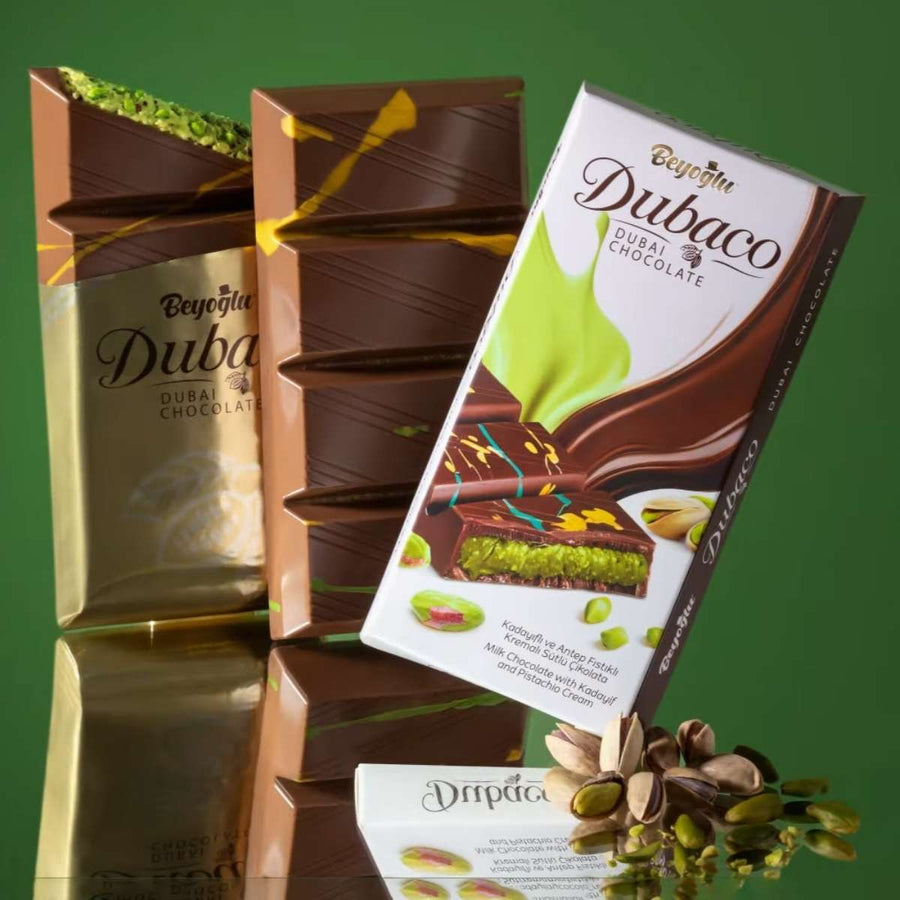 Stacked chocolate bars include one in gold wrapping and another in white packaging labeled "Dubaco," with pistachios hinting at a luscious pistachio cream filling inside the Beyoglu - Dubaco Premium Dubai Chocolate Bar - 200g.
