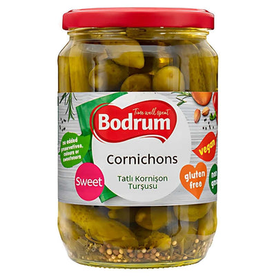 Bodrum Sweet Cornichons (680g) are pickled cucumbers with a vibrant red lid, labeled as sweet, gluten-free, vegan, and non-GMO—a perfect condiment for any meal!.
