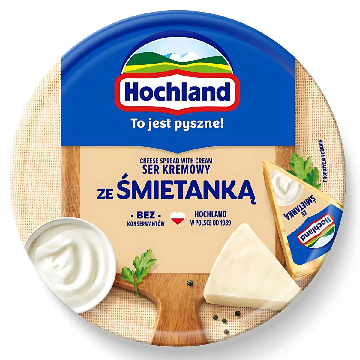 Hochland - Soft Creamy Cheese - 180g: Round container with a cheese wedge, parsley, peppercorns, and a dollop of cream on a wooden board; product text in Polish.
