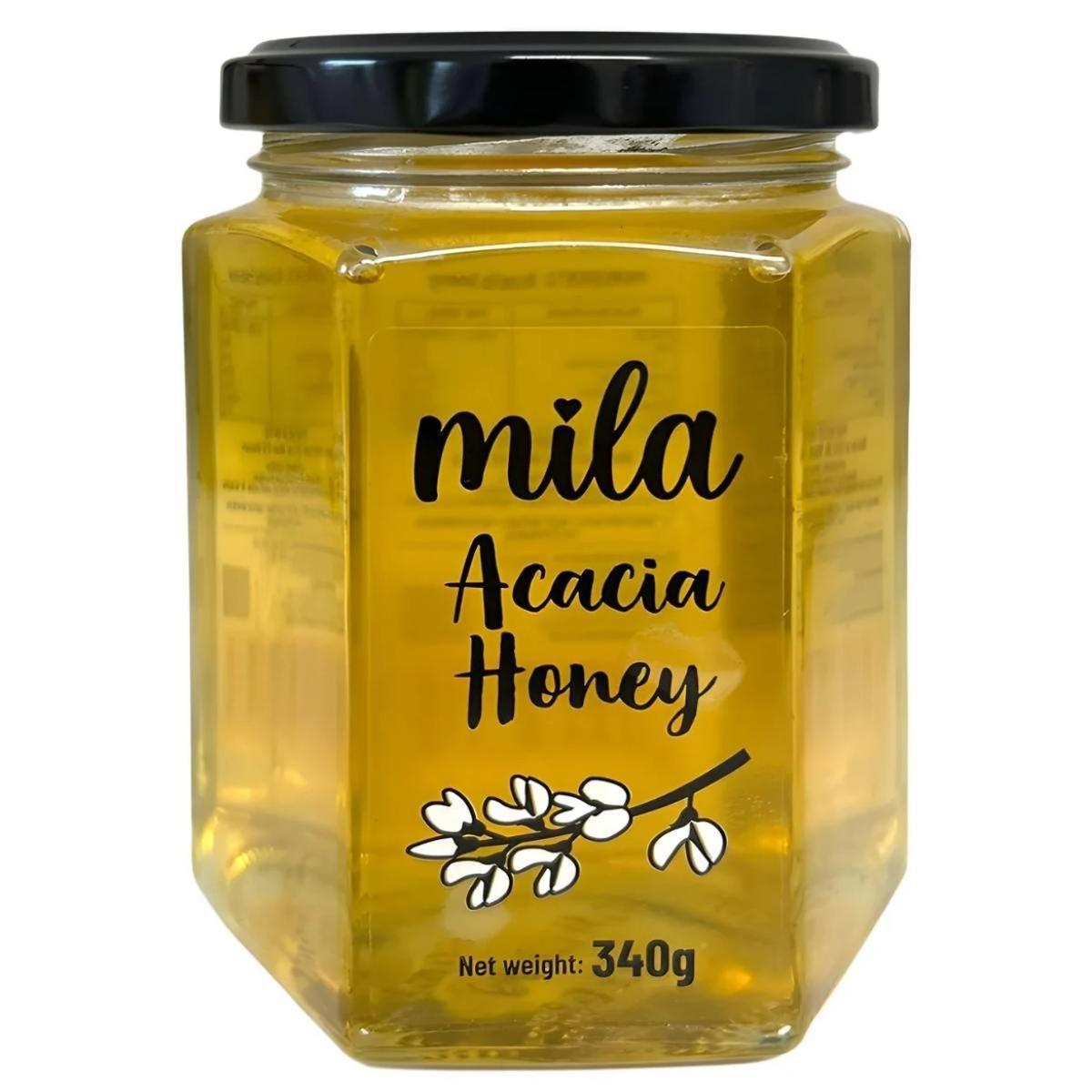 Mila - Acacia Honey with Honeycomb (340g) comes in a hexagonal glass jar with a black lid, featuring a label decorated with white acacia flowers and subtle honeycomb details.