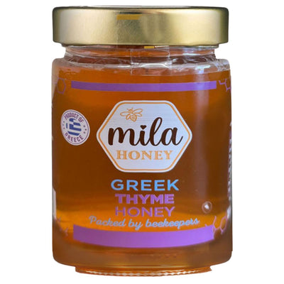 A 450g Mila Greek Thyme Honey Jar with a gold lid and purple-white label, featuring text that highlights this raw honey is packed by beekeepers in Greece.