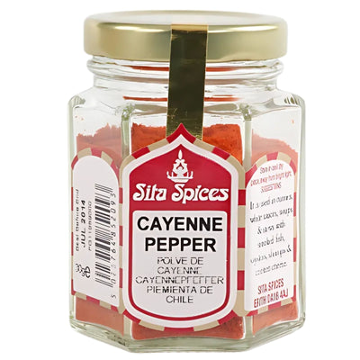 A hexagonal glass jar with a gold lid contains Sita Spices - Cayenne Pepper - 30g. The front label shows the brand name and product details in several languages.