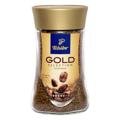 A 100g glass jar of Tchibo - Gold Selection Instant Coffee, featuring a gold lid and beige label with coffee beans and product info.